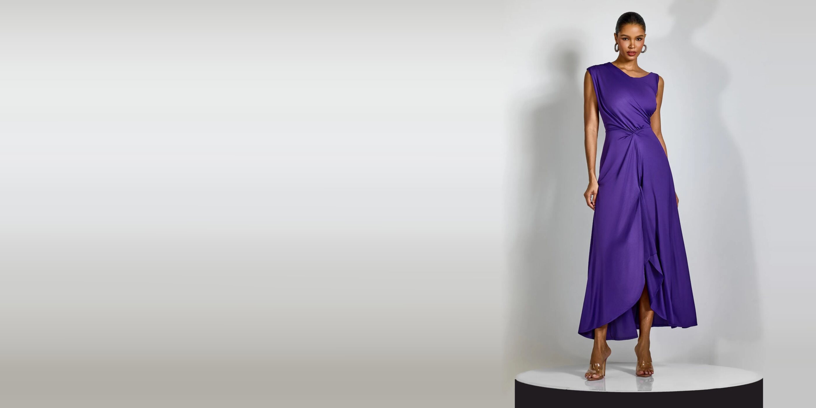 Robe longue drapée violette portée en studio, la jupe fendue retombant sur un socle